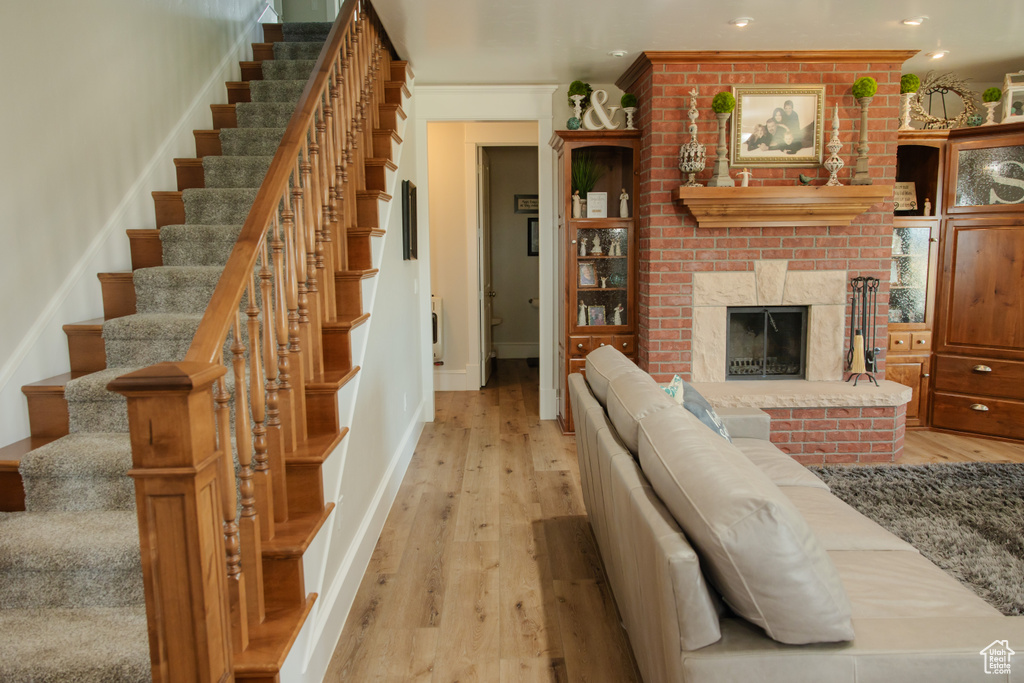 Living area featuring light wood-style floors, stairway, baseboards, recessed lighting, and a brick fireplace