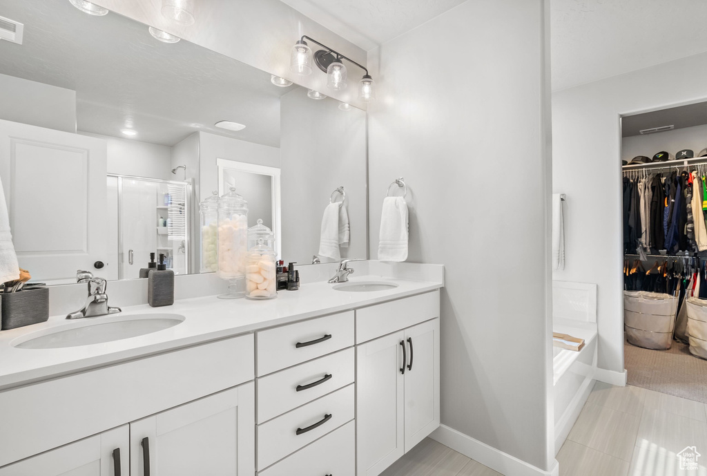 Bathroom featuring a shower stall, double vanity, a walk in closet, a bath, and baseboards
