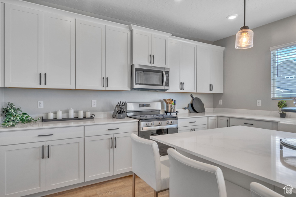 Kitchen with stainless steel appliances, light countertops, white cabinetry, hanging light fixtures, and recessed lighting