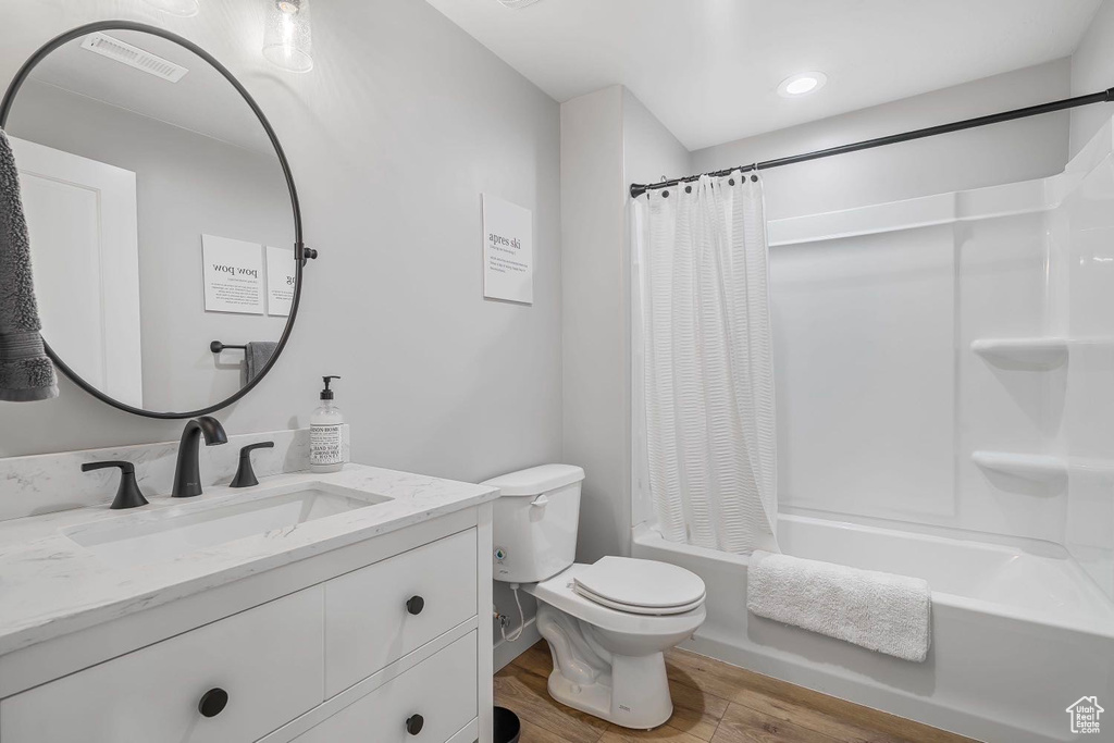 Full bath with vanity, wood finished floors, shower / bathtub combination with curtain, and toilet