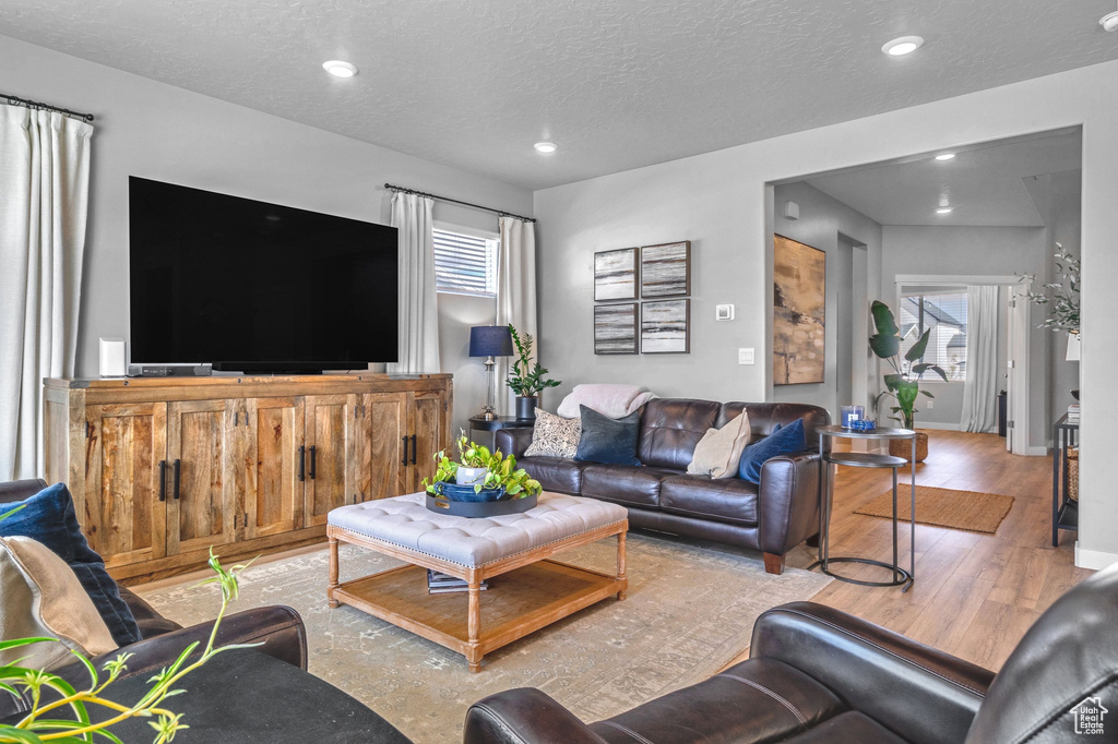 Living room featuring light wood-type flooring, recessed lighting, a textured ceiling, and baseboards