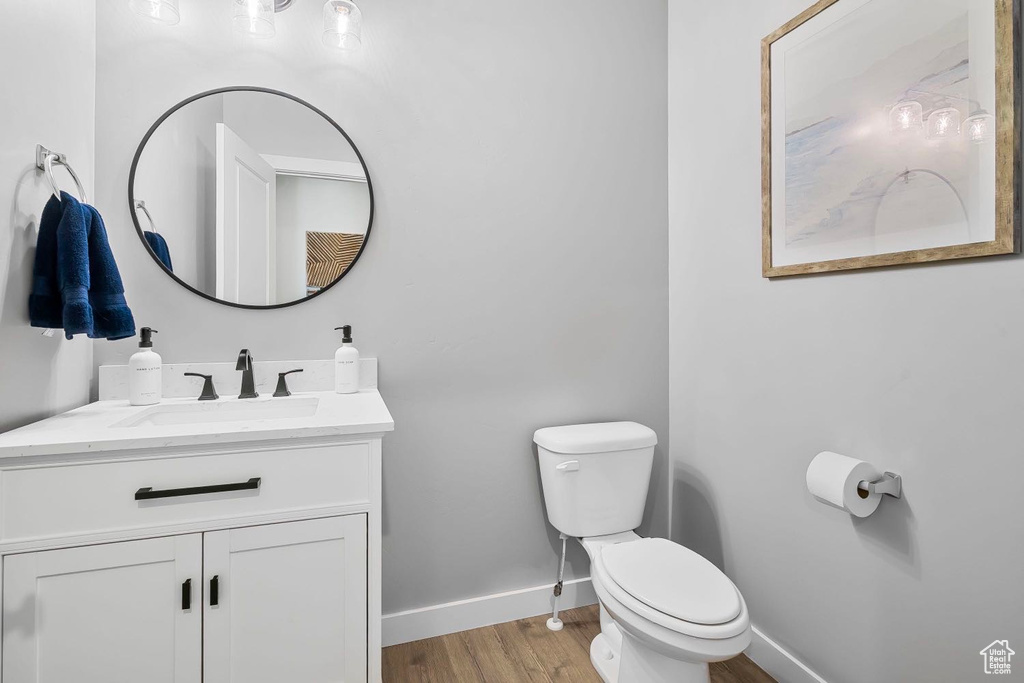 Half bathroom with toilet, wood finished floors, vanity, and baseboards