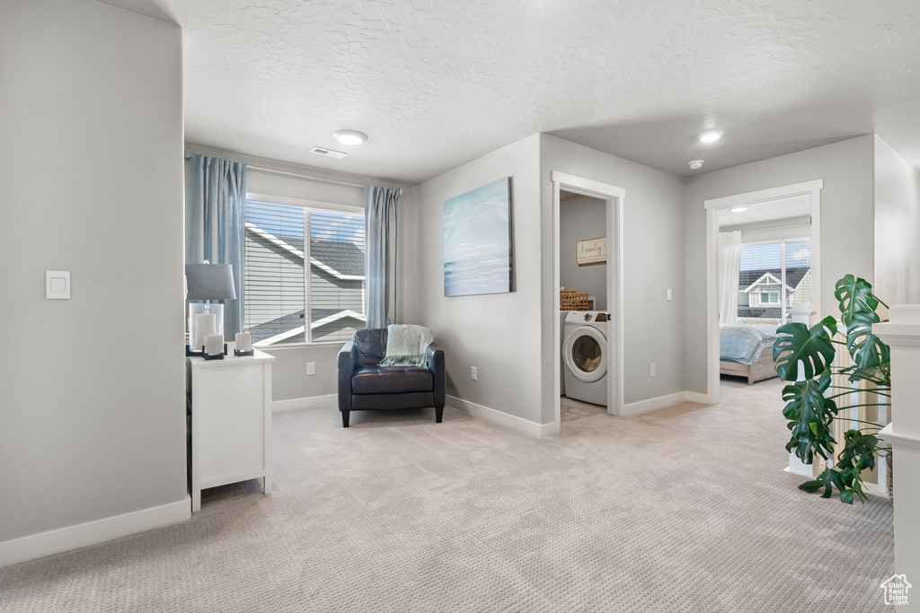 Living area with washer / dryer, light carpet, baseboards, and a textured ceiling