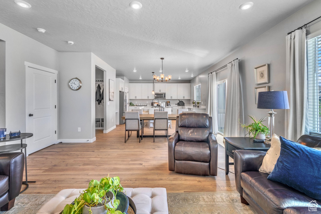Living room with a chandelier, light wood-type flooring, baseboards, a textured ceiling, and recessed lighting