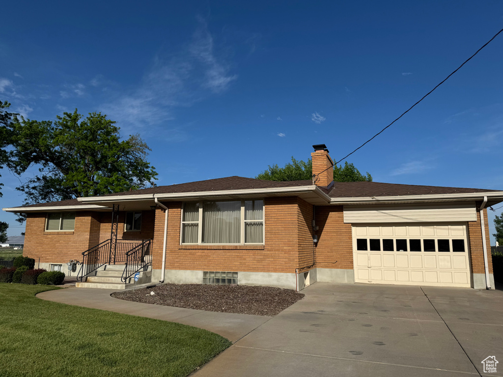 Ranch-style house featuring a garage, concrete driveway, brick siding, a chimney, and a front lawn