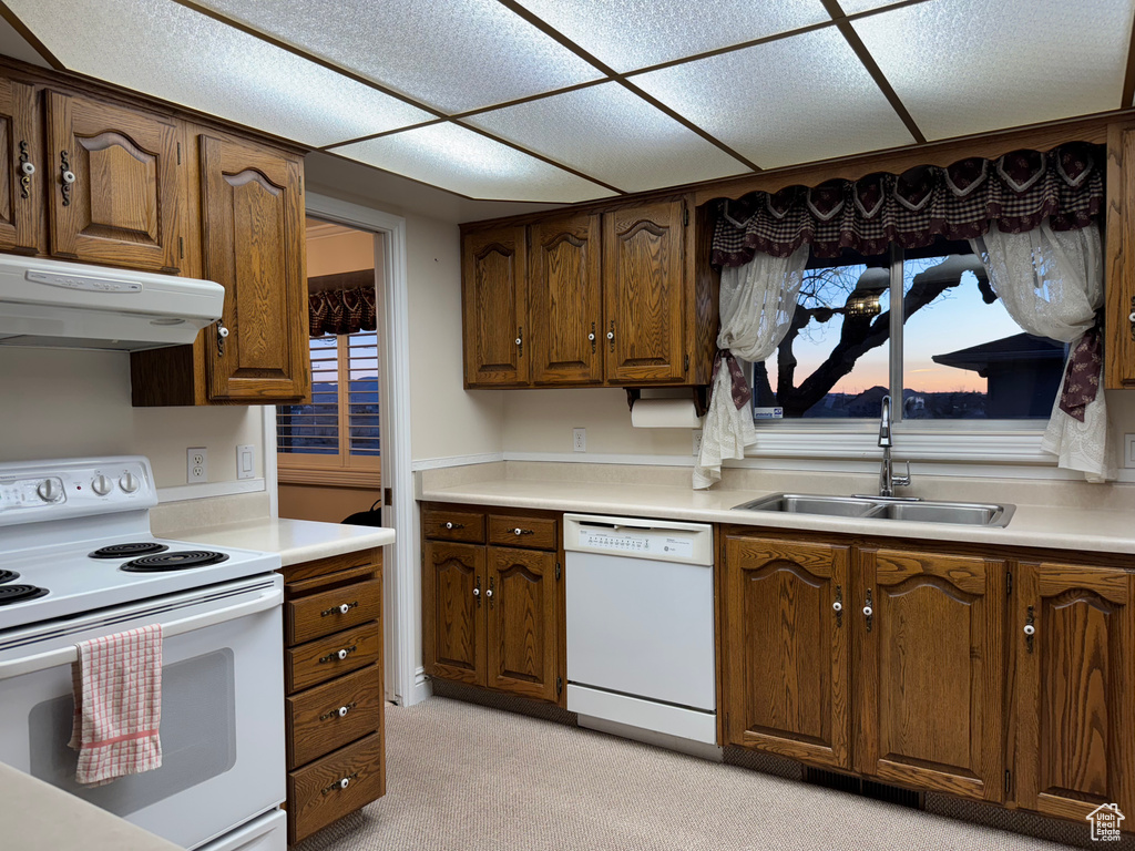 Kitchen featuring white appliances, a sink, under cabinet range hood, and light countertops
