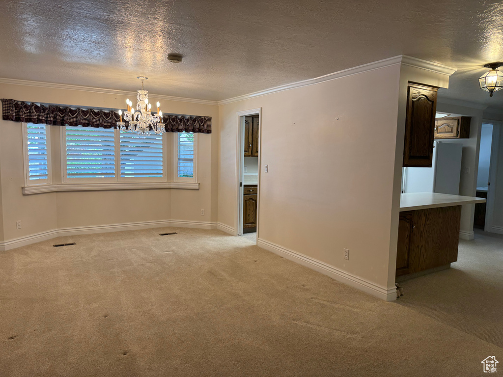 Spare room featuring a chandelier, light carpet, ornamental molding, a textured ceiling, and baseboards