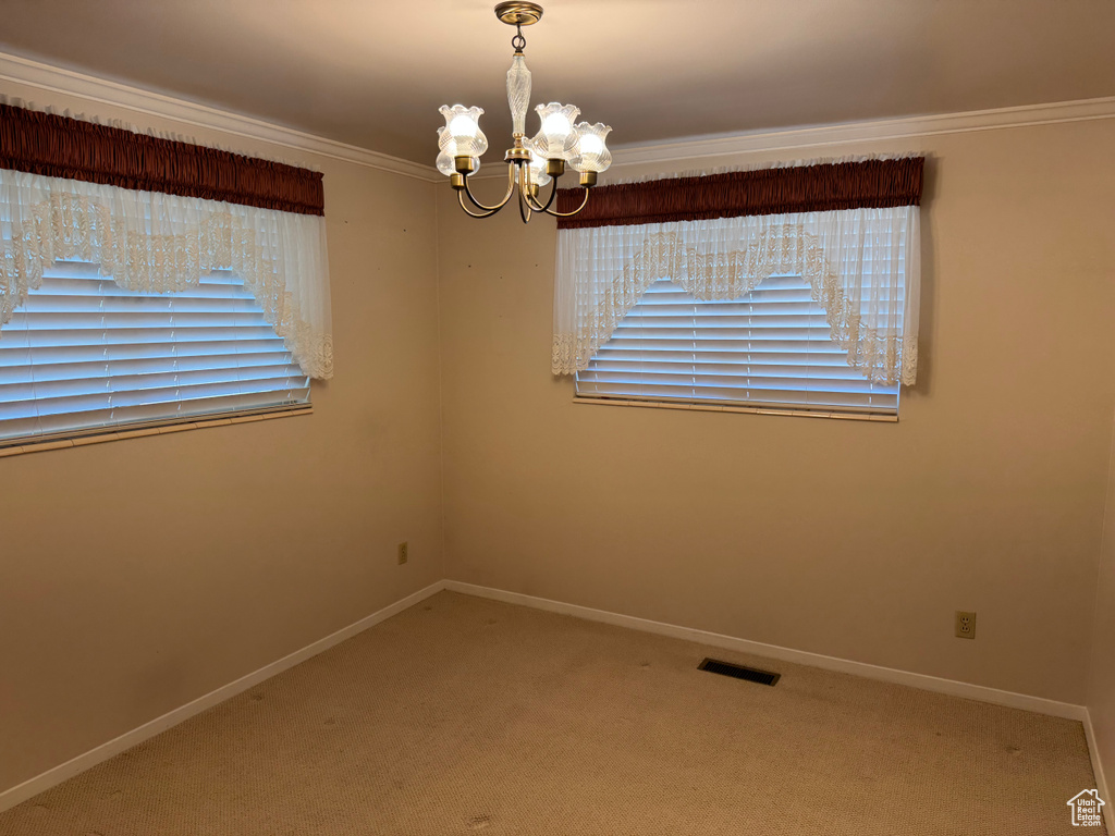 Unfurnished room featuring a chandelier, carpet, baseboards, and crown molding