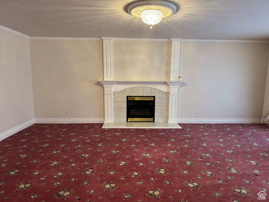 Unfurnished living room with carpet, a tiled fireplace, ornamental molding, baseboards, and a textured ceiling