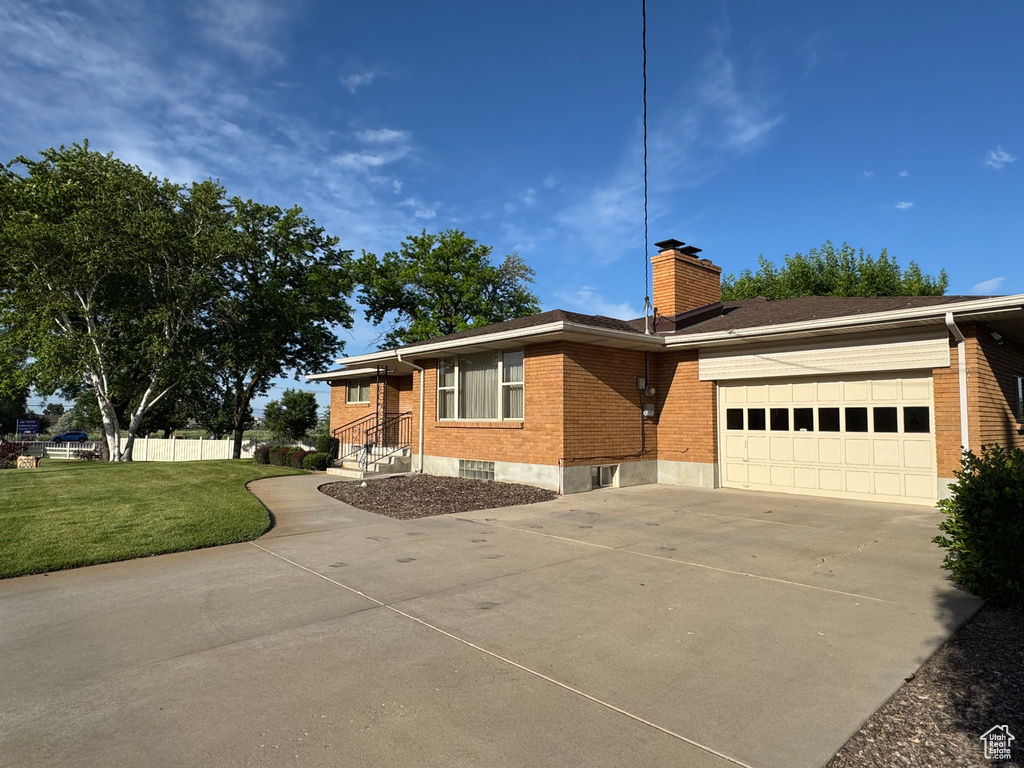 Single story home featuring concrete driveway, brick siding, an attached garage, and a chimney