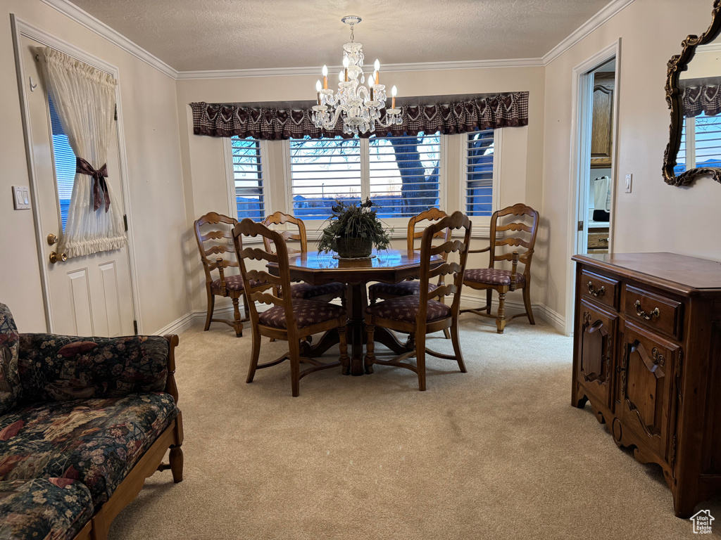Dining space with a chandelier, light carpet, crown molding, baseboards, and a textured ceiling