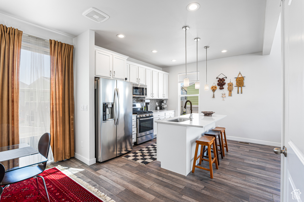 Kitchen featuring appliances with stainless steel finishes, a sink, a kitchen breakfast bar, recessed lighting, and white cabinetry