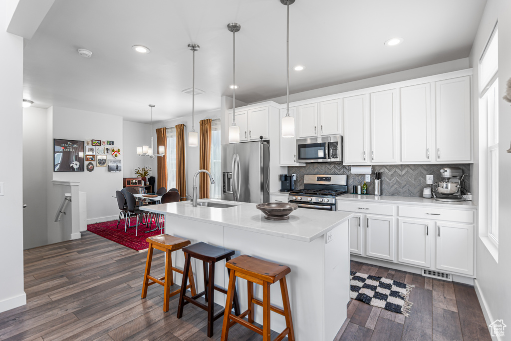 Kitchen with appliances with stainless steel finishes, a sink, dark wood-style flooring, tasteful backsplash, and a center island with sink