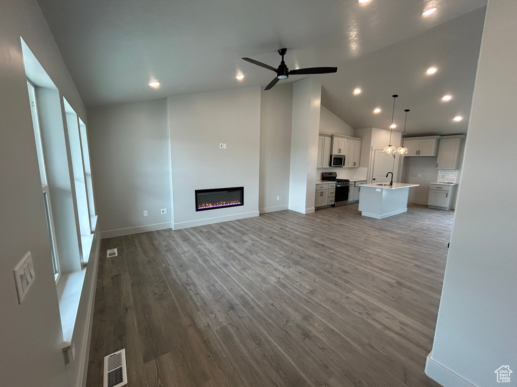 Unfurnished living room featuring a sink, vaulted ceiling, a glass covered fireplace, wood finished floors, and recessed lighting