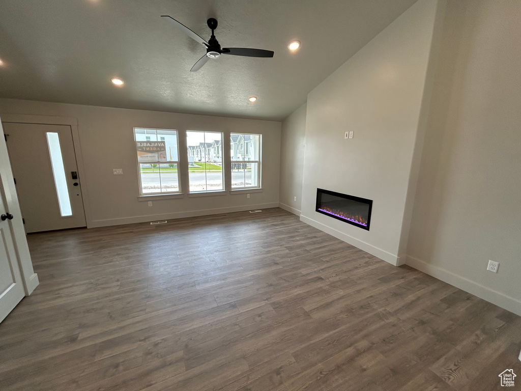 Unfurnished living room featuring baseboards, wood finished floors, a glass covered fireplace, recessed lighting, and lofted ceiling