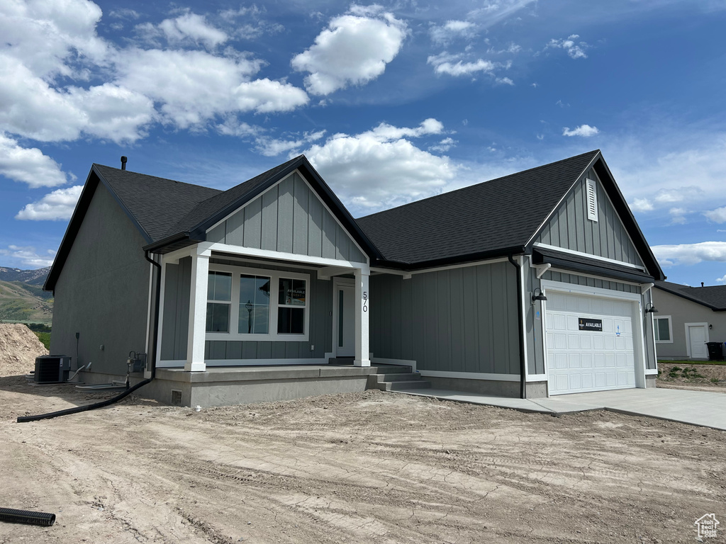 Modern farmhouse style home featuring concrete driveway, a garage, covered porch, central AC unit, and roof with shingles