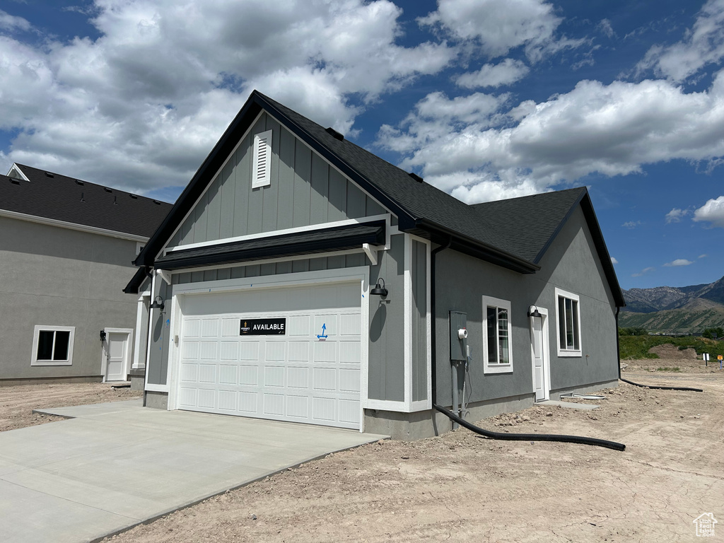 View of front facade featuring concrete driveway, board and batten siding, a mountain view, an attached garage, and a shingled roof