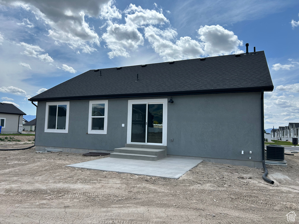 Back of house featuring a shingled roof, stucco siding, cooling unit, and a patio area