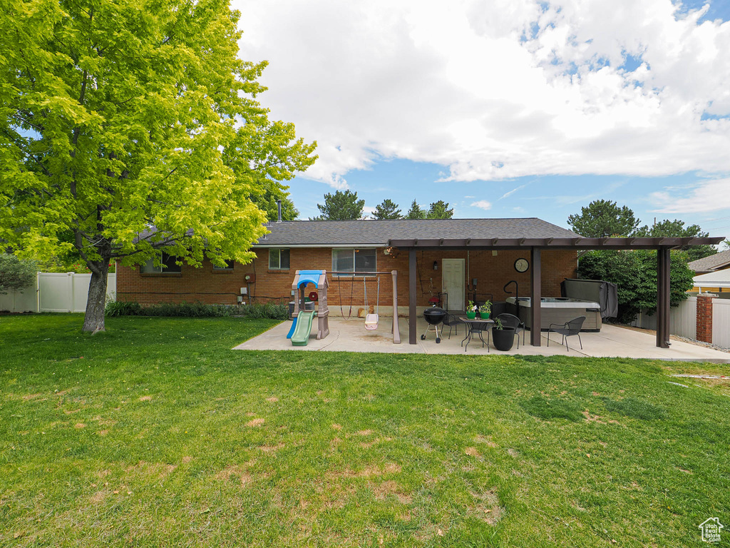 Back of property featuring a patio, a hot tub, brick siding, and a playground