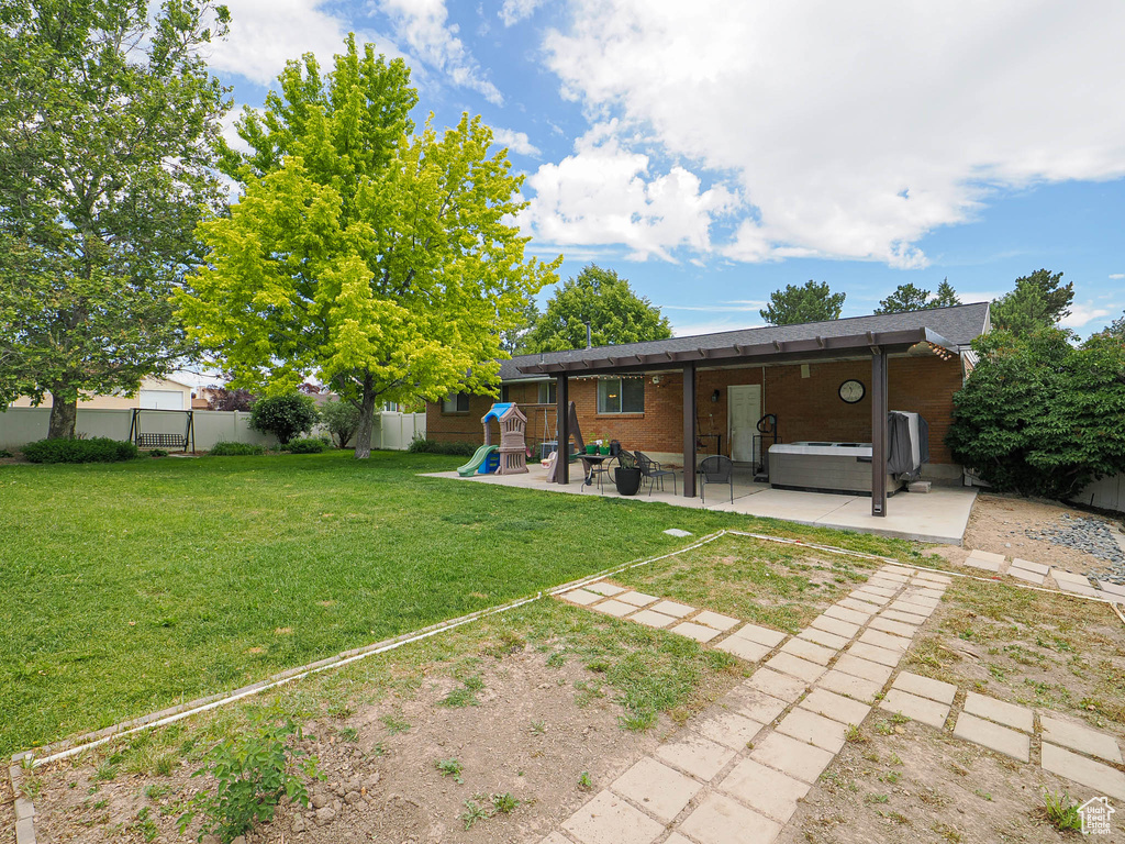 View of yard with a hot tub, a playground, and a patio area