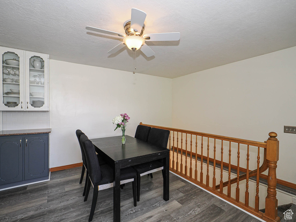 Dining area featuring dark wood-style flooring, ceiling fan, baseboards, and a textured ceiling