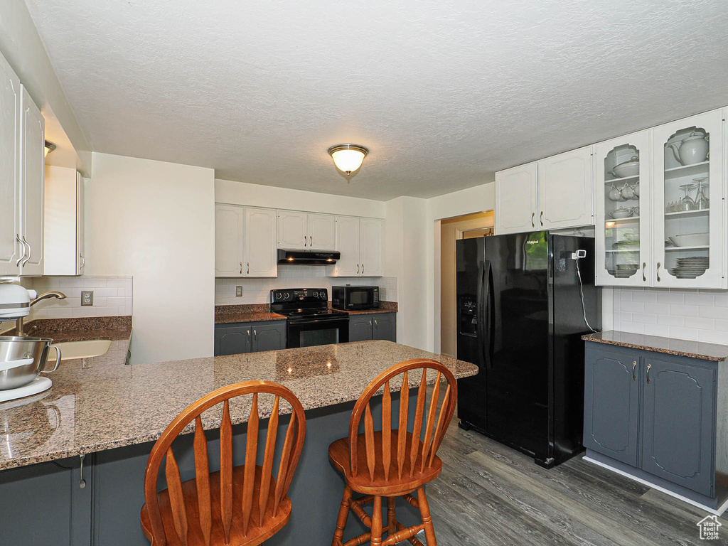 Kitchen featuring black appliances, a sink, under cabinet range hood, a peninsula, and white cabinets