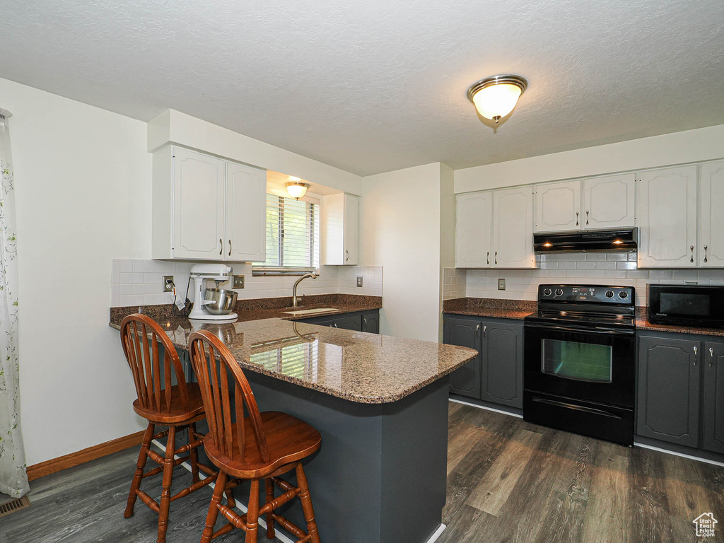 Kitchen with black appliances, under cabinet range hood, a sink, a kitchen bar, and dark wood-type flooring