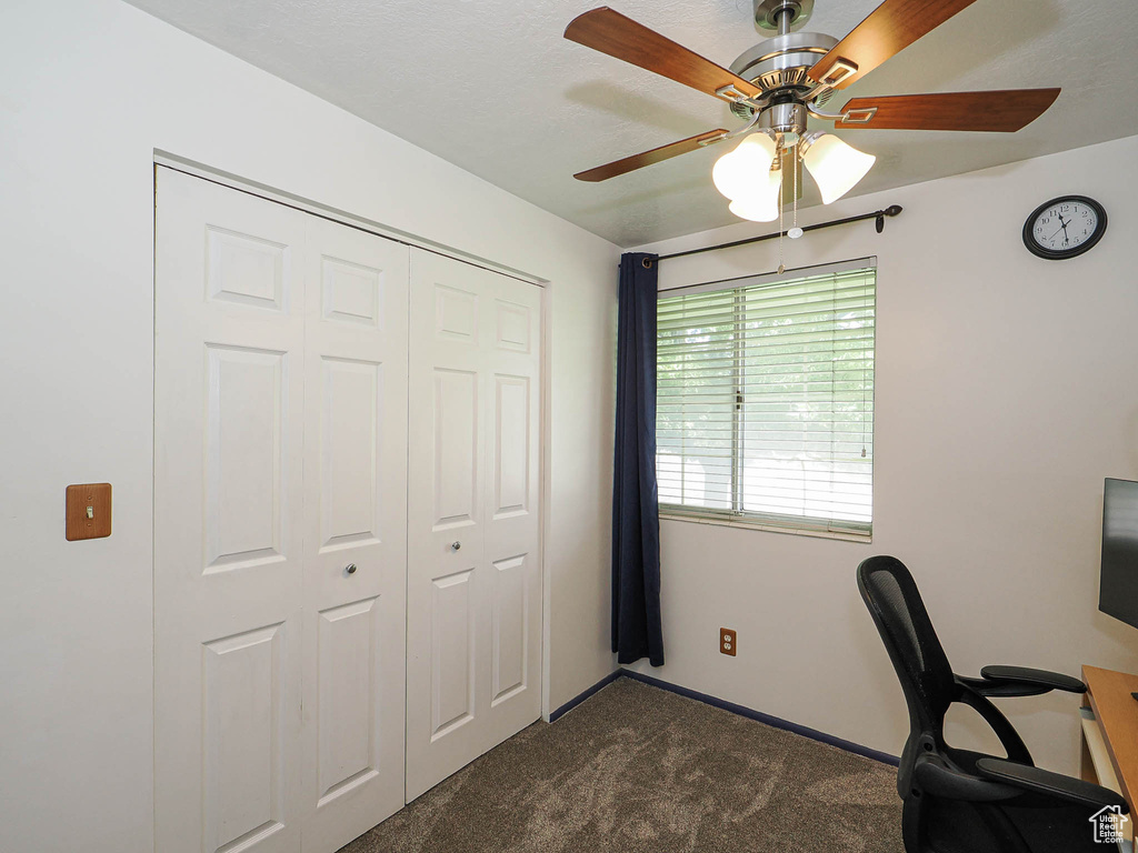 Office space with dark carpet, ceiling fan, and baseboards