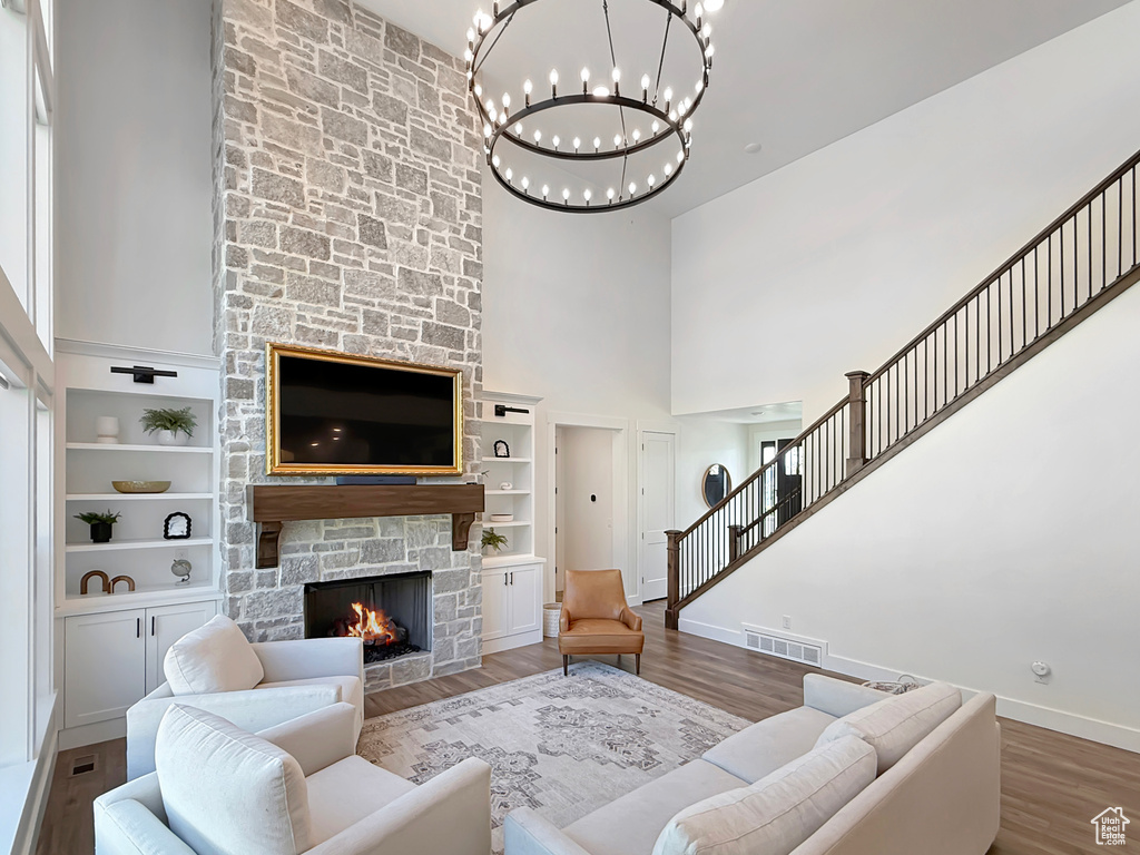 Living area featuring a towering ceiling, baseboards, a chandelier, a stone fireplace, and wood finished floors