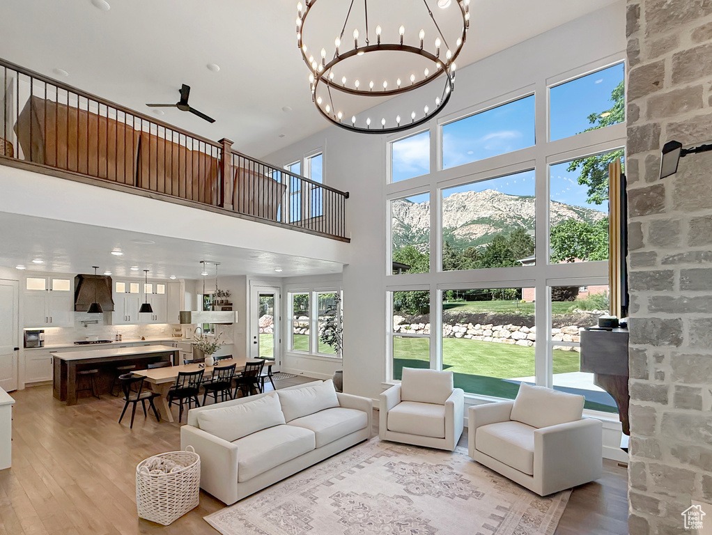 Living room with light wood-type flooring, a high ceiling, a ceiling fan, recessed lighting, and a chandelier