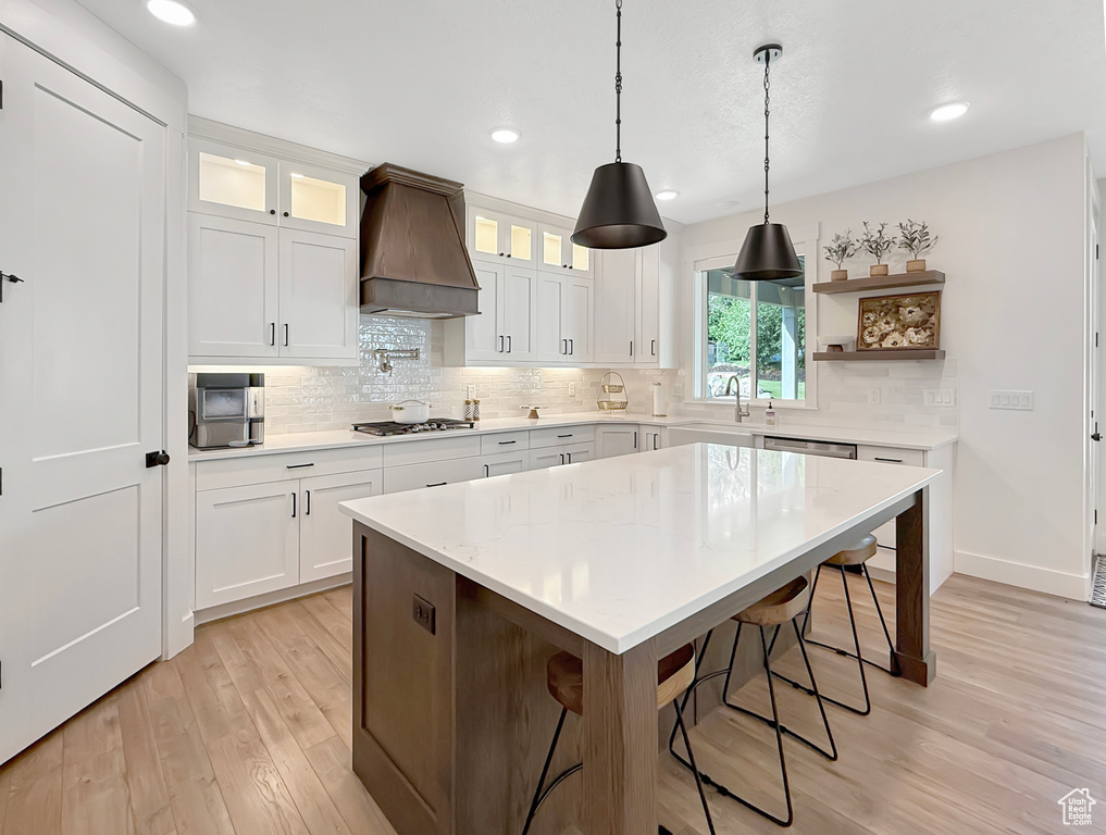 Kitchen featuring custom range hood, light wood-style floors, a sink, backsplash, and a kitchen breakfast bar