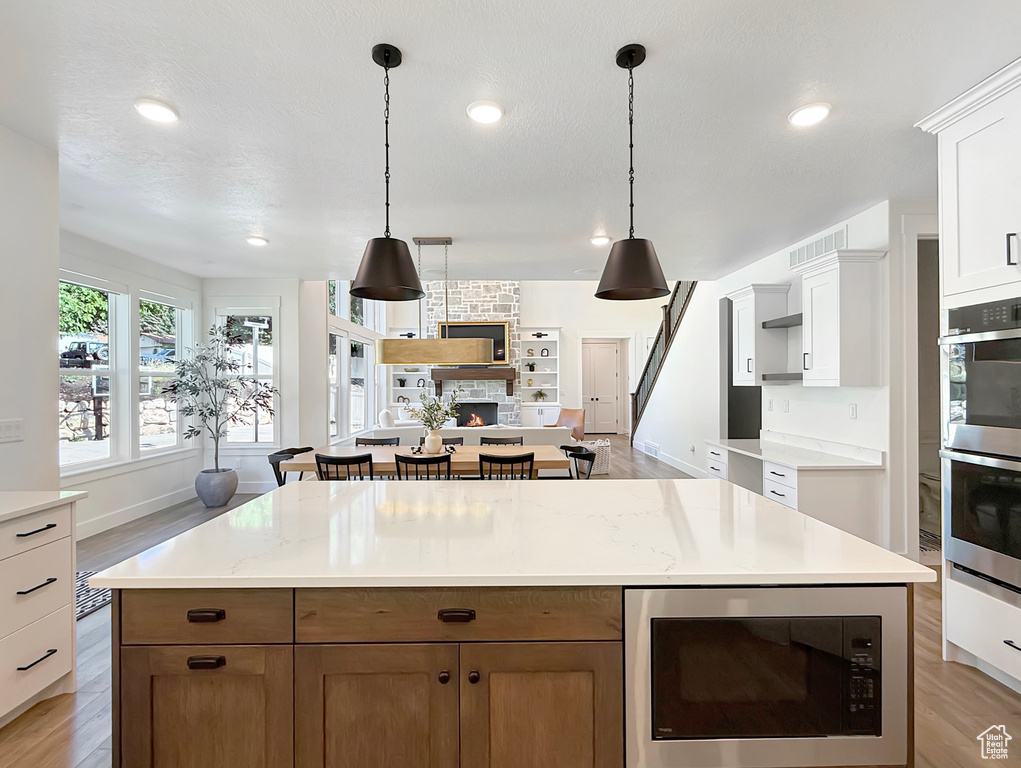 Kitchen with built in microwave, light wood-type flooring, stainless steel double oven, hanging light fixtures, and recessed lighting