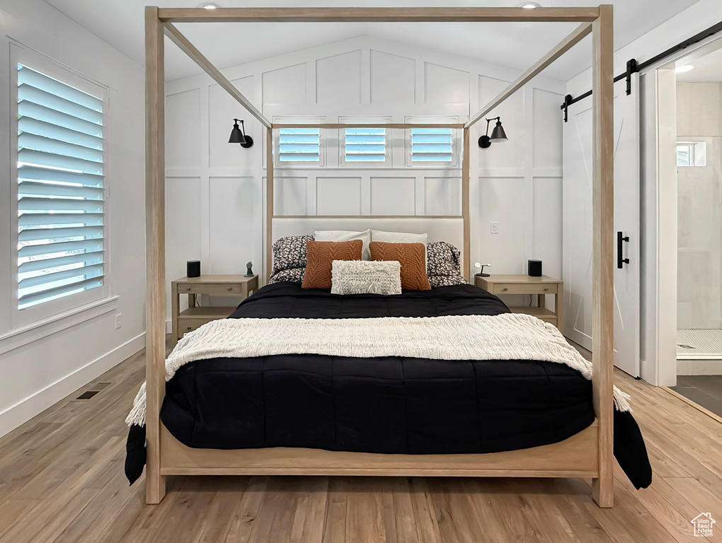 Bedroom featuring a barn door, a decorative wall, light wood finished floors, and baseboards