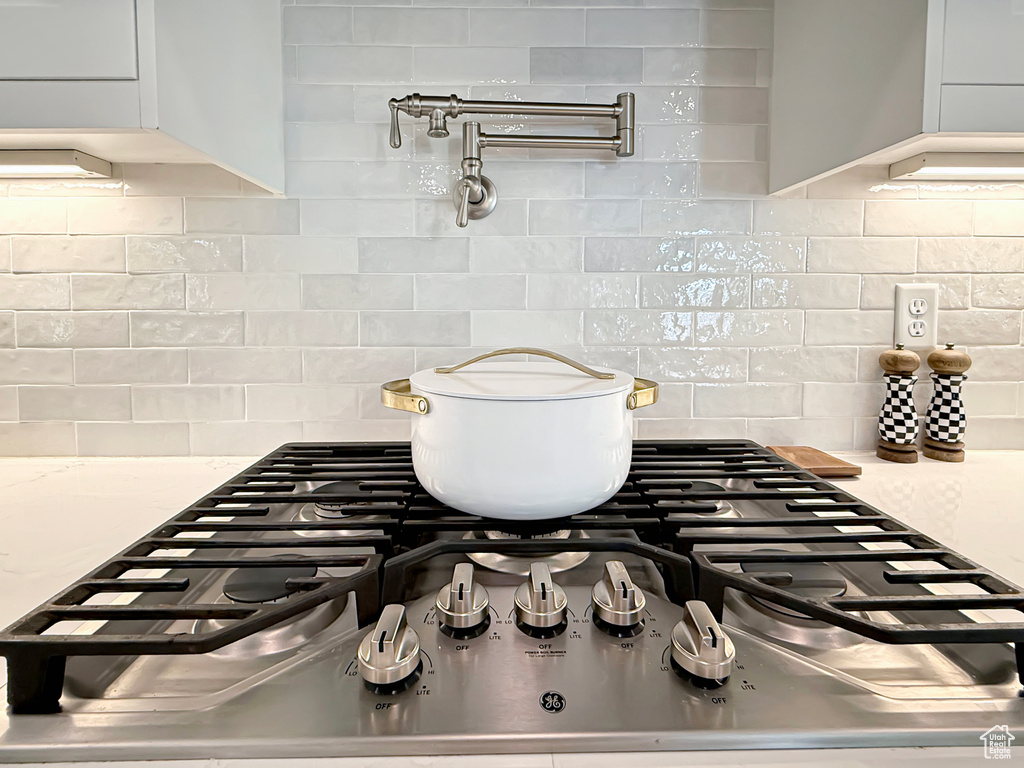Kitchen view of pot filler, tasteful backsplash, and stainless steel gas stovetop