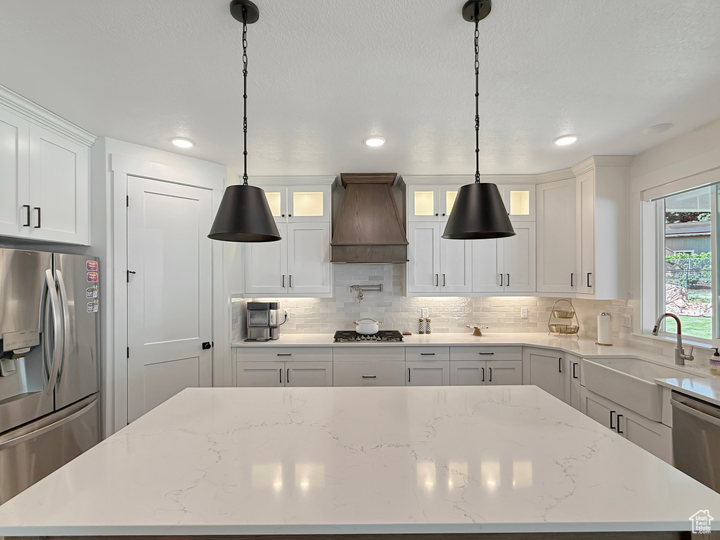 Kitchen featuring stainless steel appliances, premium range hood, a kitchen island, white cabinets, and a sink