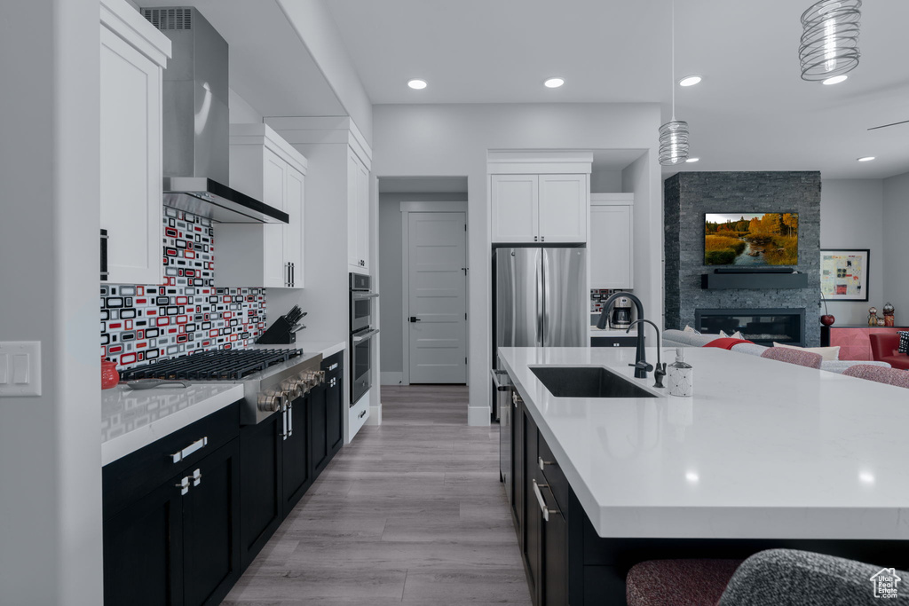 Kitchen featuring wall chimney range hood, stainless steel appliances, dark cabinetry, a sink, and light countertops
