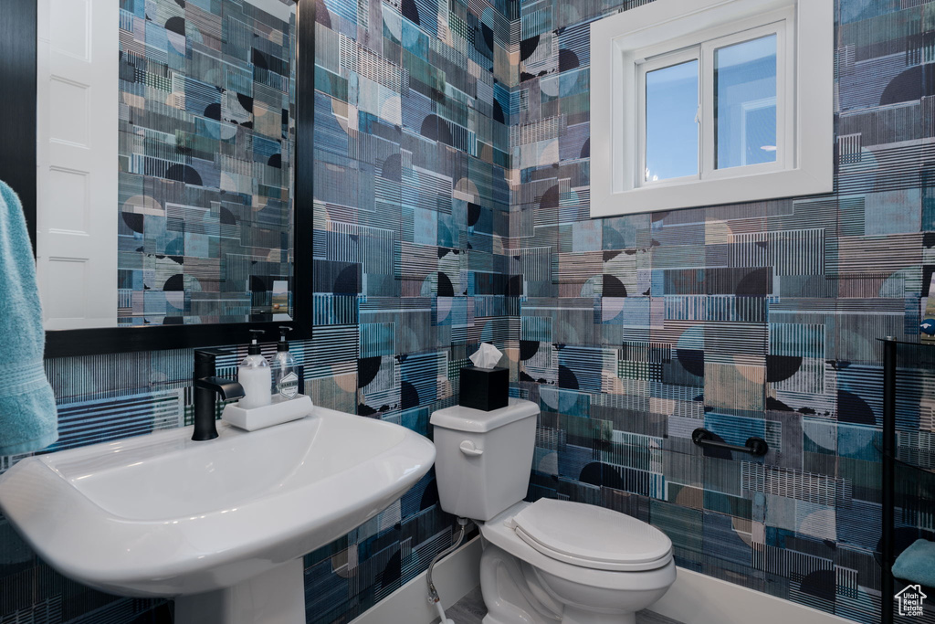 Half bathroom with tile walls, a sink, toilet, and backsplash