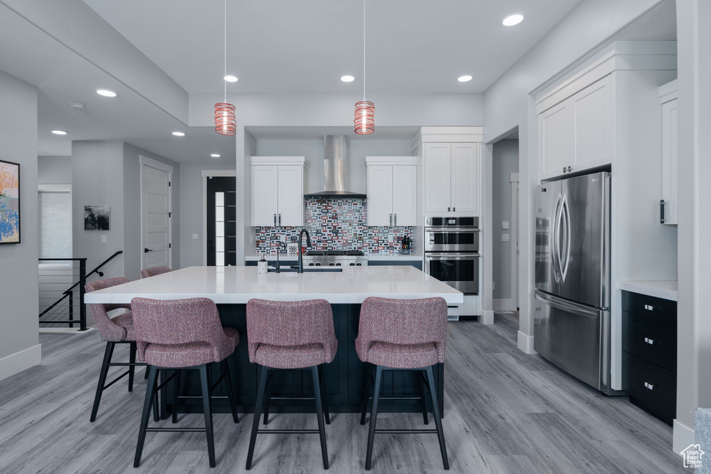 Kitchen featuring appliances with stainless steel finishes, wall chimney range hood, light wood-type flooring, a sink, and recessed lighting
