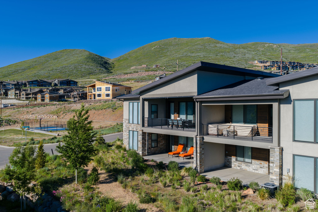 Back of property featuring stone siding, stucco siding, a balcony, and a patio