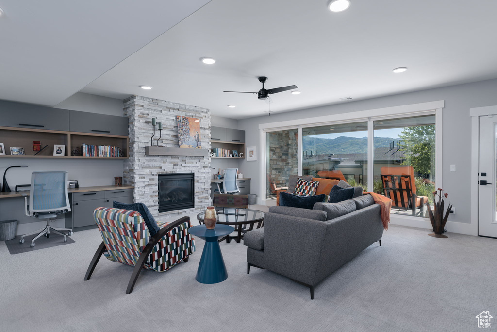 Living room featuring a stone fireplace, light carpet, ceiling fan, a desk, and recessed lighting