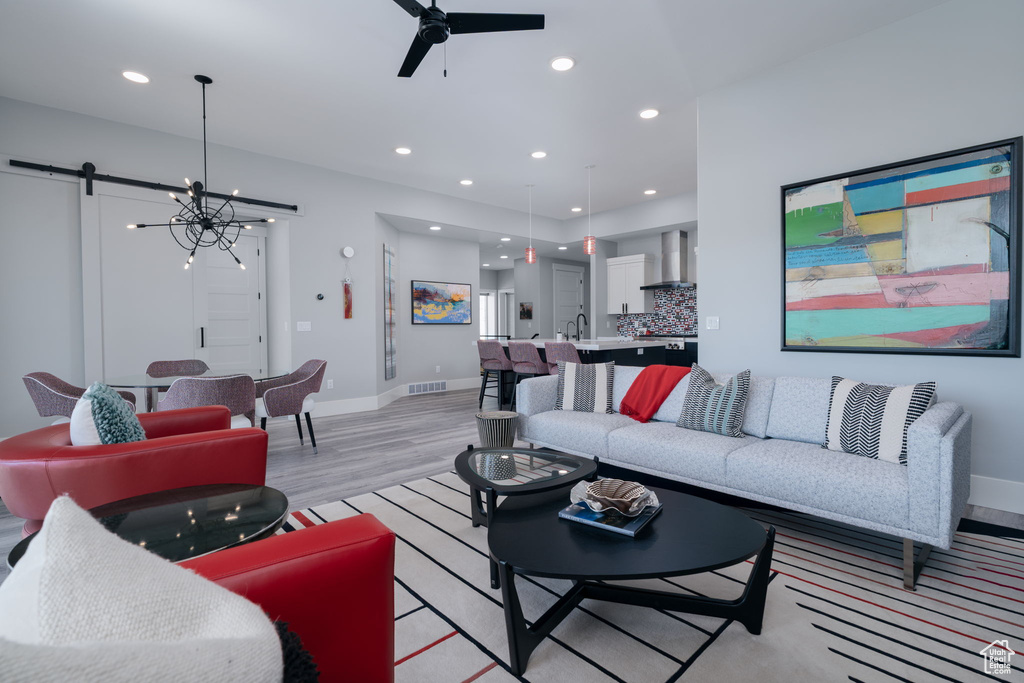 Living area featuring light wood-style floors, a ceiling fan, baseboards, recessed lighting, and a chandelier