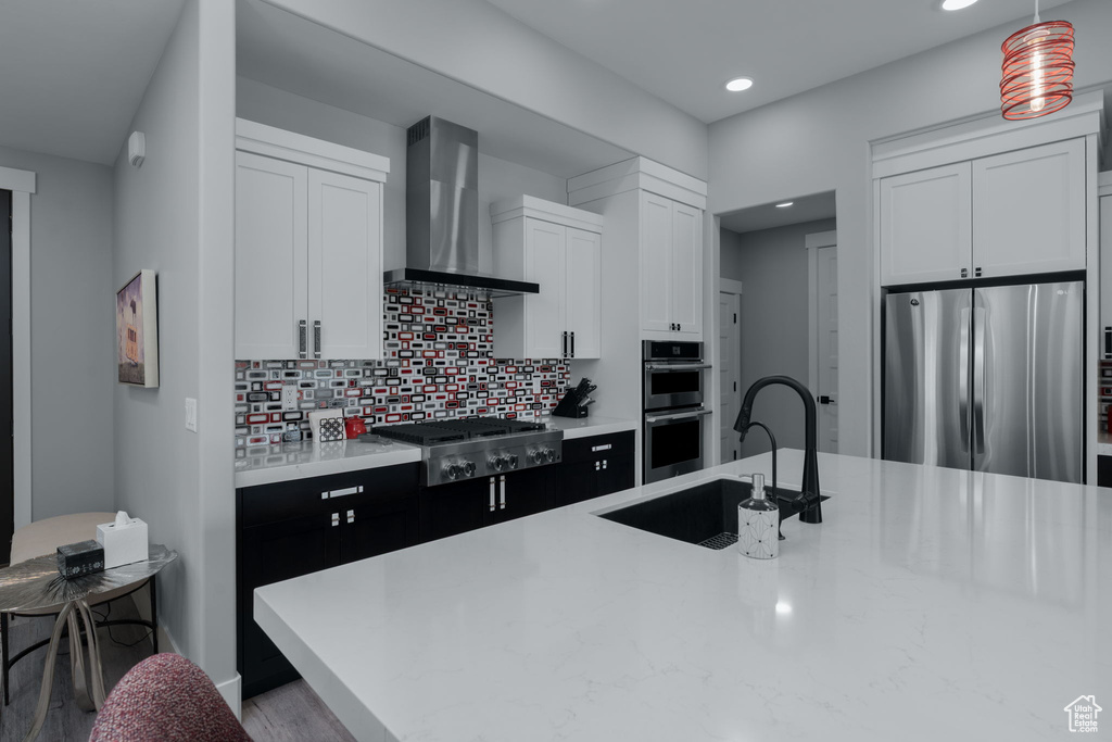 Kitchen featuring appliances with stainless steel finishes, wall chimney exhaust hood, a sink, recessed lighting, and light countertops
