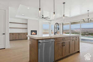 Kitchen featuring dishwasher, a chandelier, hanging light fixtures, light countertops, and an island with sink