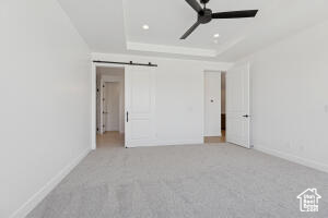 Unfurnished bedroom with a barn door, a tray ceiling, carpet floors, recessed lighting, and a ceiling fan