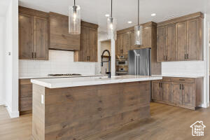Kitchen featuring freestanding refrigerator, light wood-type flooring, light countertops, pendant lighting, and recessed lighting