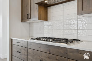 Kitchen featuring stainless steel gas cooktop, backsplash, ventilation hood, and light countertops