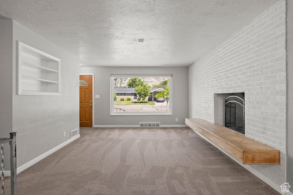 Unfurnished living room with carpet, a textured ceiling, a brick fireplace, baseboards, and built in features