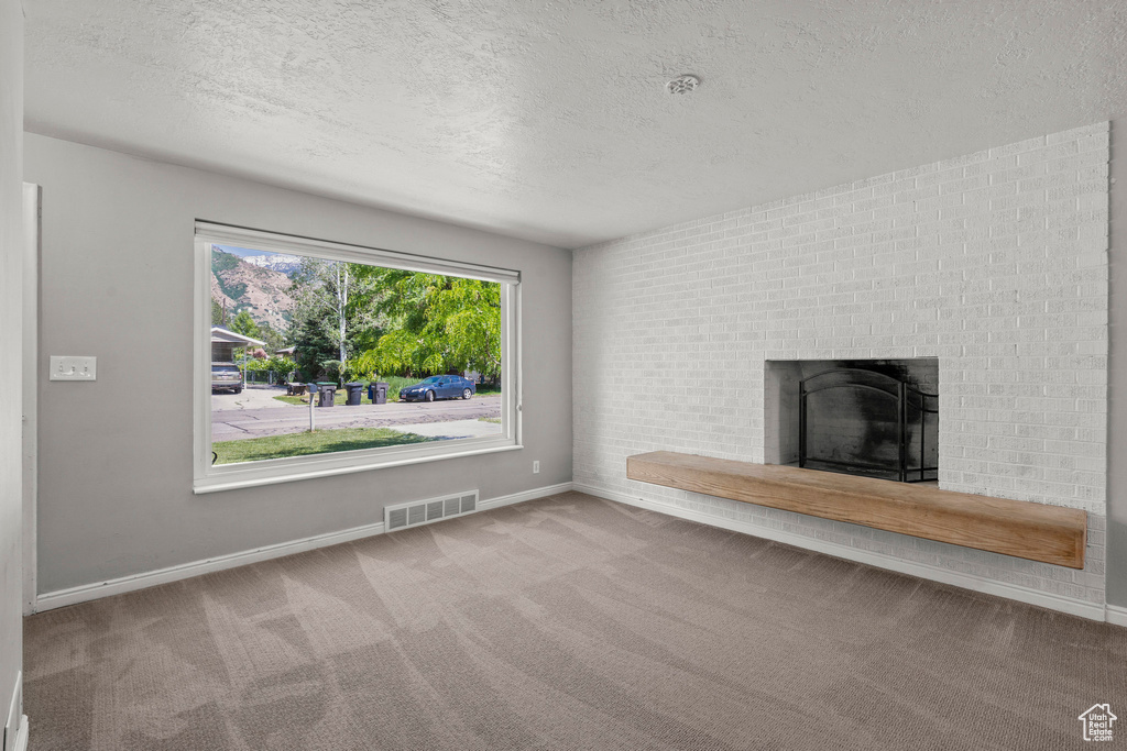 Unfurnished living room featuring a textured ceiling, carpet flooring, a brick fireplace, and baseboards