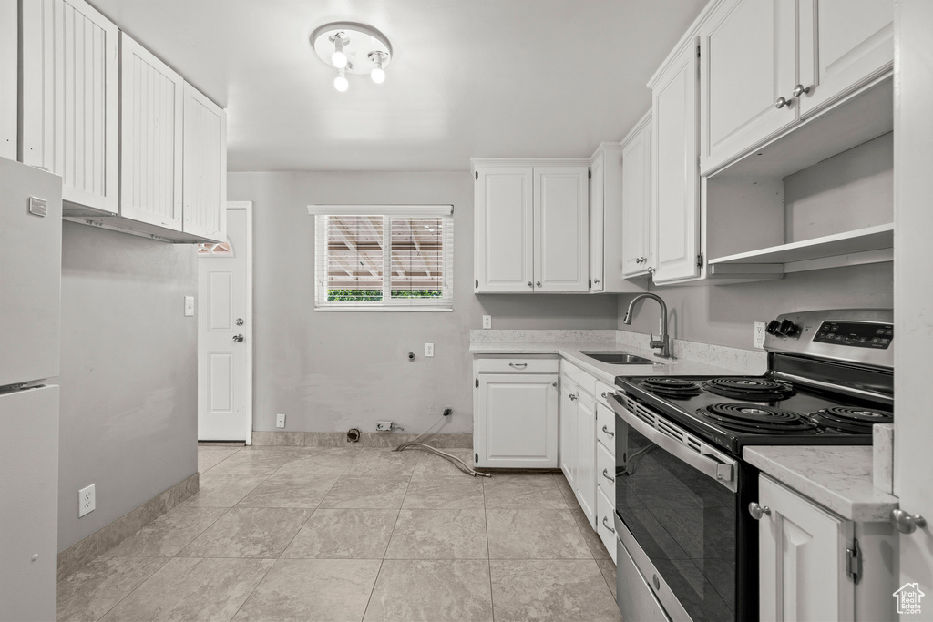 Kitchen featuring electric range, a sink, light countertops, freestanding refrigerator, and white cabinetry