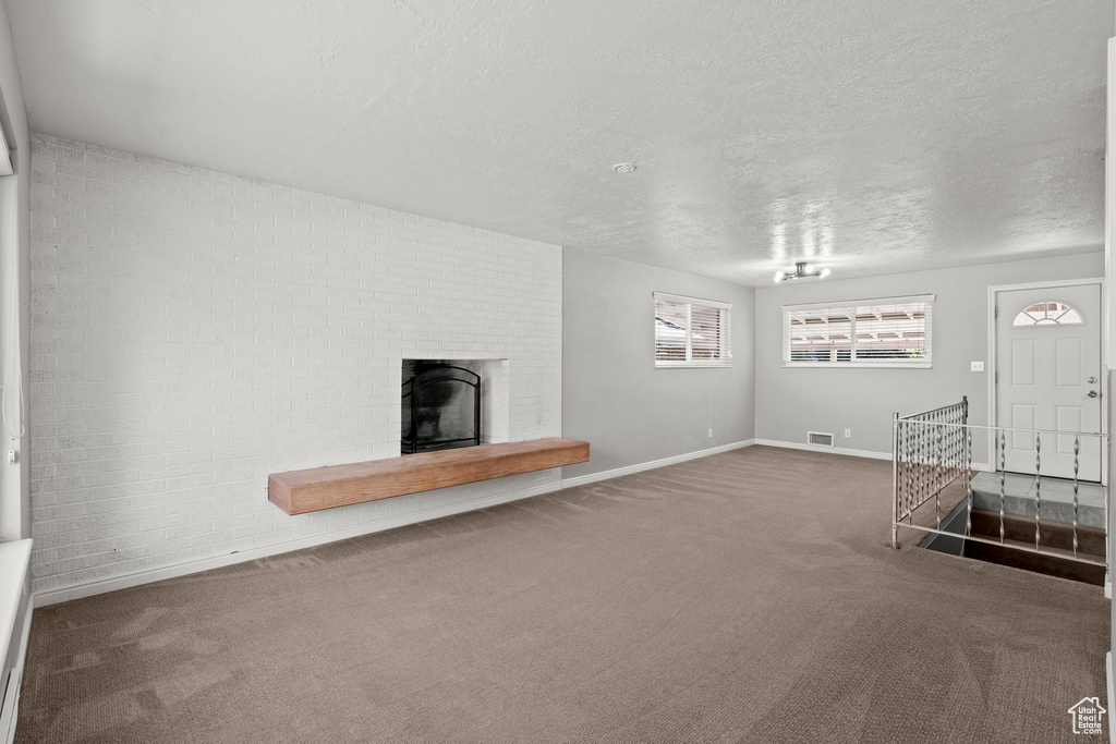Unfurnished living room with carpet floors, baseboards, a fireplace, and a textured ceiling